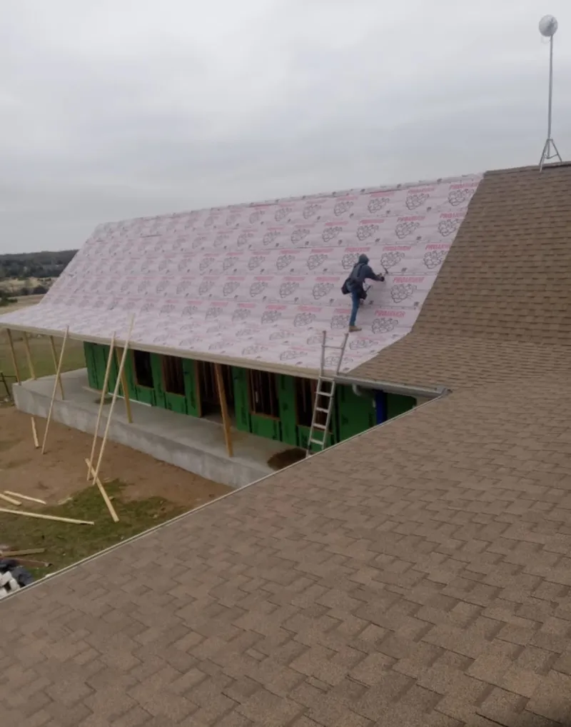 Worker preparing underlayment for a metal roof installation in Troy